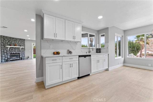 kitchen featuring white cabinets, light wood-type flooring, stainless steel dishwasher, and a fireplace