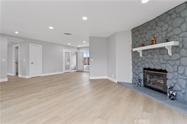 unfurnished living room with a stone fireplace and light hardwood / wood-style floors