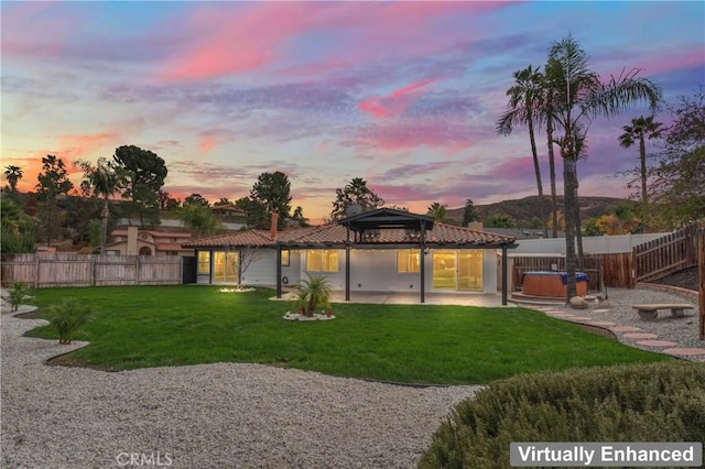 back house at dusk featuring a gazebo, a patio area, a yard, and a hot tub