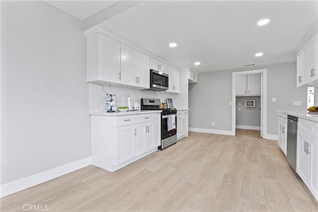 kitchen with appliances with stainless steel finishes, light hardwood / wood-style flooring, white cabinetry, and tasteful backsplash