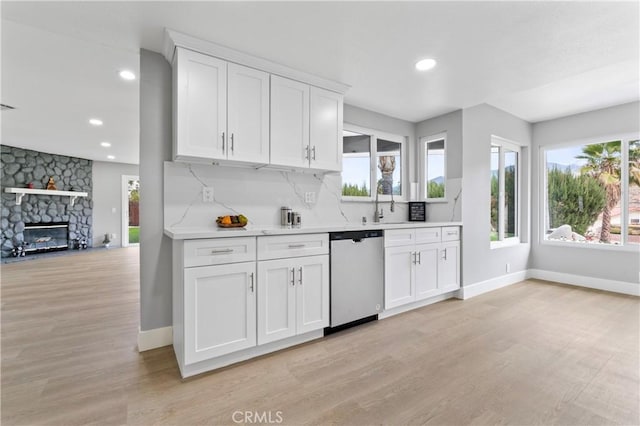 kitchen with white cabinetry, dishwasher, a stone fireplace, light hardwood / wood-style flooring, and backsplash