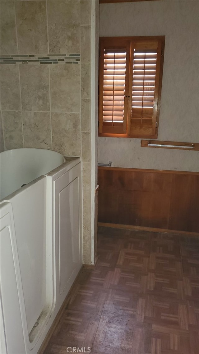 bathroom with parquet flooring, a tub to relax in, and separate washer and dryer