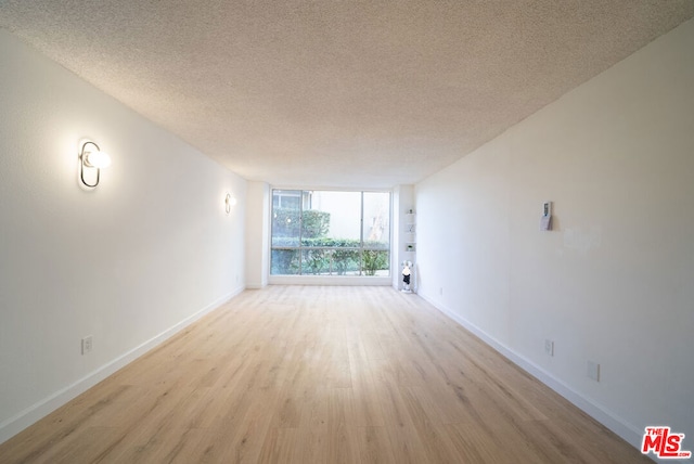 spare room with a wall of windows, a textured ceiling, and light wood-type flooring