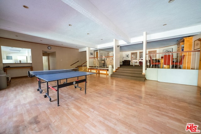 game room with a textured ceiling, light hardwood / wood-style floors, and beam ceiling