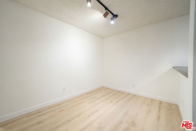 empty room featuring track lighting, light hardwood / wood-style floors, and a textured ceiling