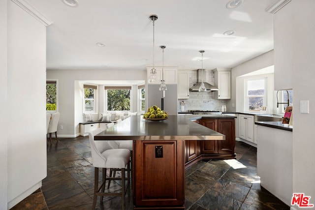 kitchen with pendant lighting, a breakfast bar, wall chimney range hood, sink, and a kitchen island