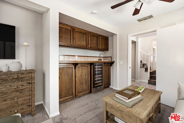 bar featuring light colored carpet, wine cooler, and ceiling fan