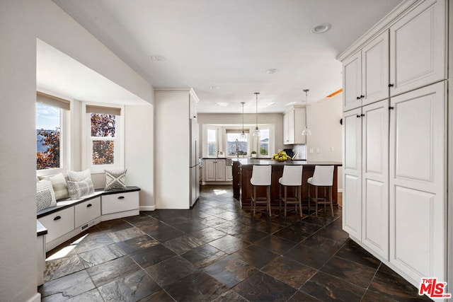 kitchen with white cabinets, a healthy amount of sunlight, a breakfast bar area, and hanging light fixtures