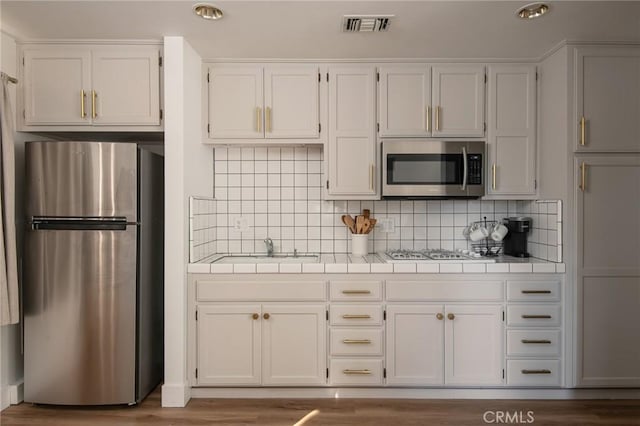 kitchen with decorative backsplash, wood-type flooring, white cabinetry, and appliances with stainless steel finishes