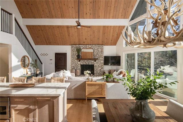 living room featuring beam ceiling, a stone fireplace, wood ceiling, and light wood-type flooring