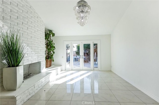 unfurnished living room with french doors, vaulted ceiling, light tile patterned floors, an inviting chandelier, and a fireplace