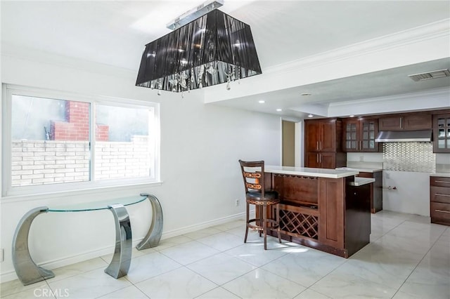 kitchen featuring backsplash, a breakfast bar, dark brown cabinets, and ornamental molding