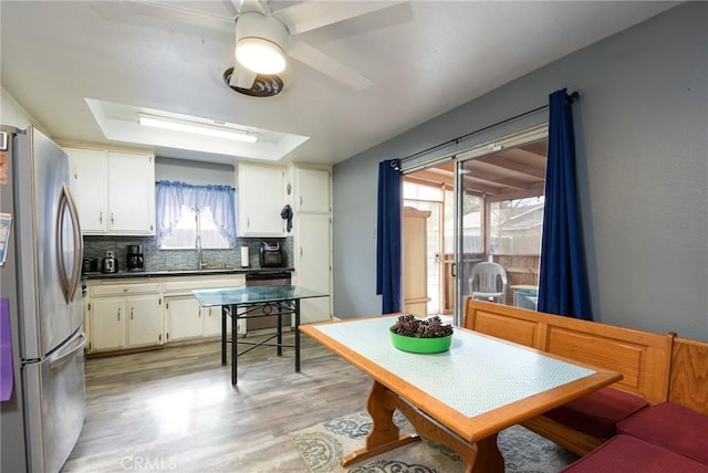 kitchen with stainless steel refrigerator, tasteful backsplash, a raised ceiling, light hardwood / wood-style floors, and white cabinets