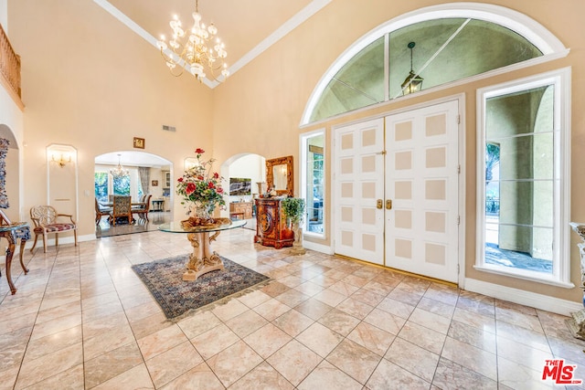 foyer featuring light tile patterned flooring, ornamental molding, a high ceiling, and an inviting chandelier