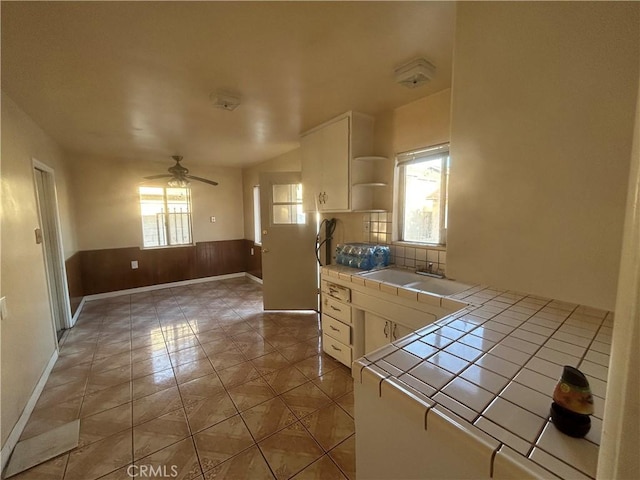 kitchen featuring ceiling fan, tile counters, sink, tile patterned floors, and white cabinets