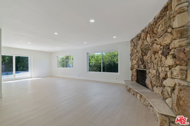 unfurnished living room with a stone fireplace and light wood-type flooring