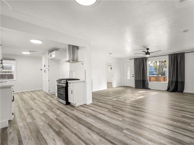 kitchen with ceiling fan, stainless steel range with gas stovetop, white cabinets, exhaust hood, and light wood-type flooring