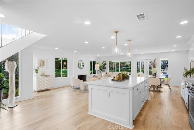 kitchen featuring french doors, light wood-type flooring, decorative light fixtures, white cabinets, and a center island