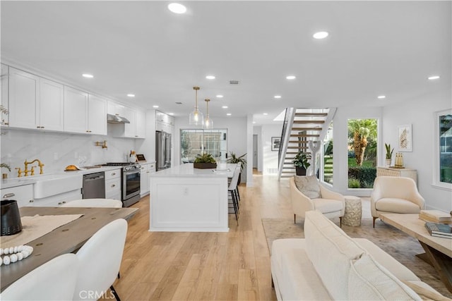 kitchen with appliances with stainless steel finishes, light wood-type flooring, pendant lighting, white cabinets, and a kitchen island