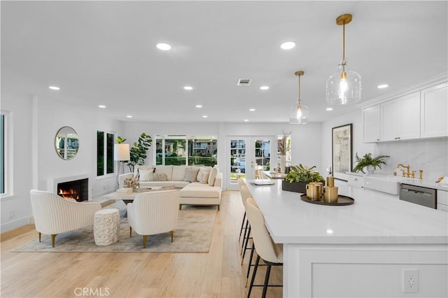 kitchen with pendant lighting, dishwasher, white cabinets, a kitchen breakfast bar, and light hardwood / wood-style flooring