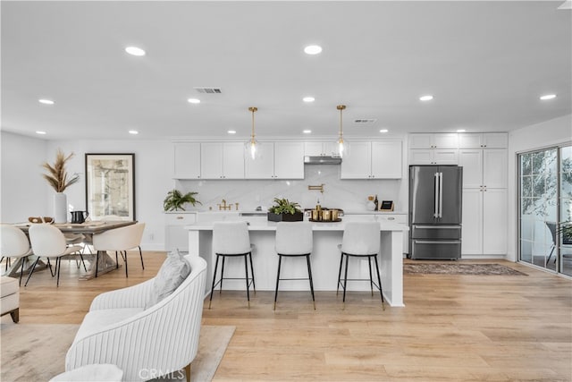 kitchen with high end refrigerator, white cabinetry, hanging light fixtures, and a kitchen breakfast bar