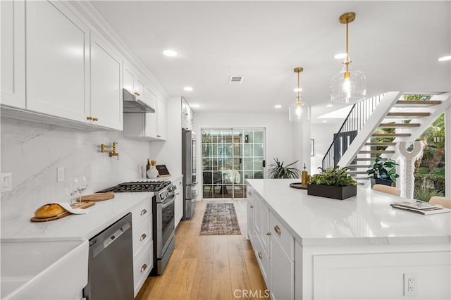 kitchen with light wood-type flooring, backsplash, stainless steel appliances, decorative light fixtures, and white cabinetry