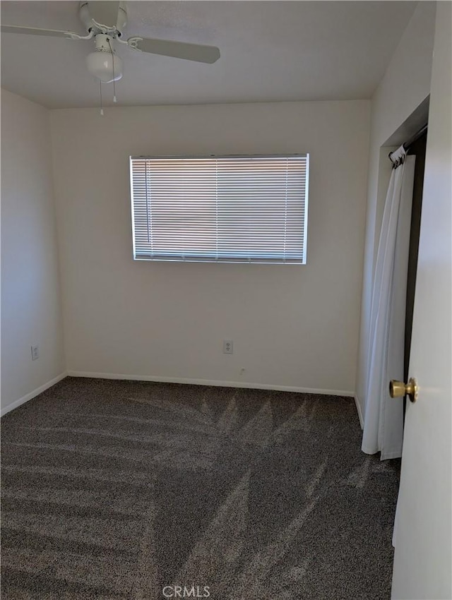 empty room featuring ceiling fan and dark carpet