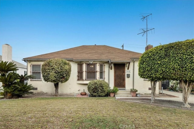 view of front of property with roof with shingles, a front yard, and stucco siding