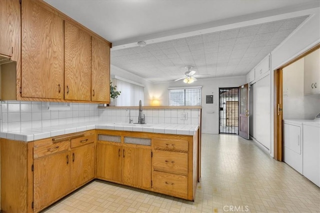 kitchen featuring tile countertops, washing machine and dryer, brown cabinetry, and a sink