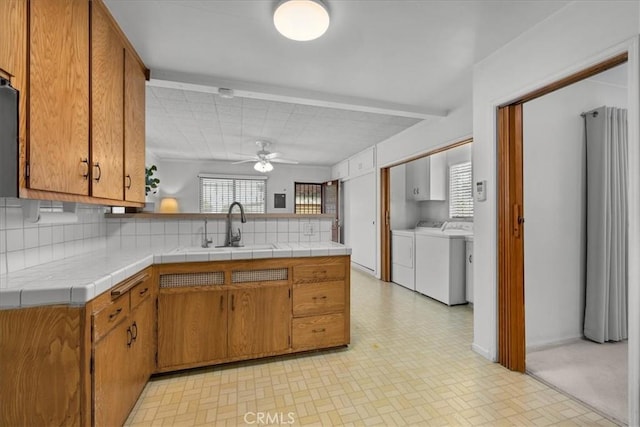 kitchen with independent washer and dryer, a sink, tile counters, and brown cabinets