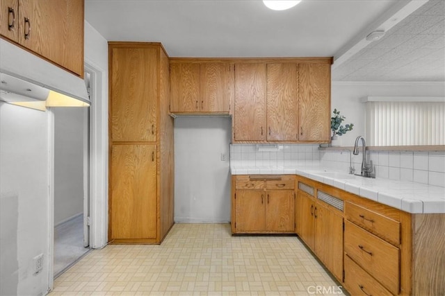 kitchen featuring tile countertops, decorative backsplash, brown cabinets, and a sink