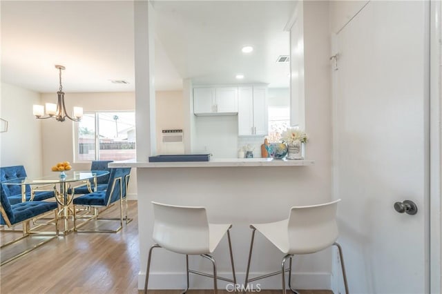 kitchen with tasteful backsplash, kitchen peninsula, a breakfast bar area, white cabinets, and a chandelier