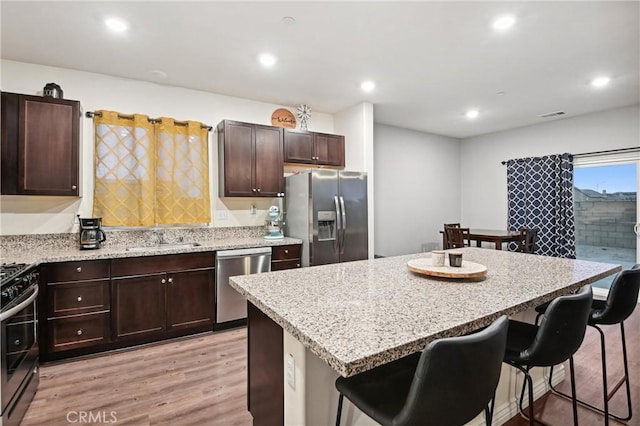 kitchen with a kitchen bar, light wood-type flooring, stainless steel appliances, sink, and a center island