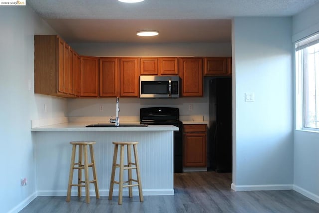 kitchen with kitchen peninsula, a breakfast bar, sink, black appliances, and wood-type flooring