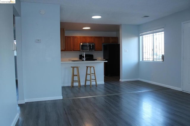 kitchen featuring black refrigerator, a kitchen bar, kitchen peninsula, and dark wood-type flooring