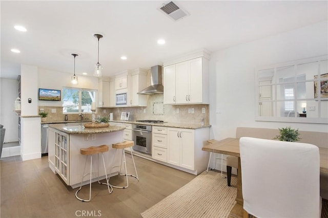 kitchen with white cabinets, decorative light fixtures, stainless steel appliances, and wall chimney range hood