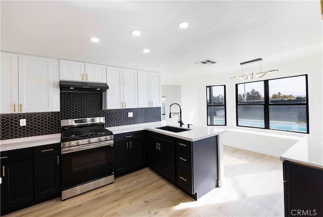 kitchen featuring pendant lighting, white cabinets, stainless steel gas range, sink, and kitchen peninsula