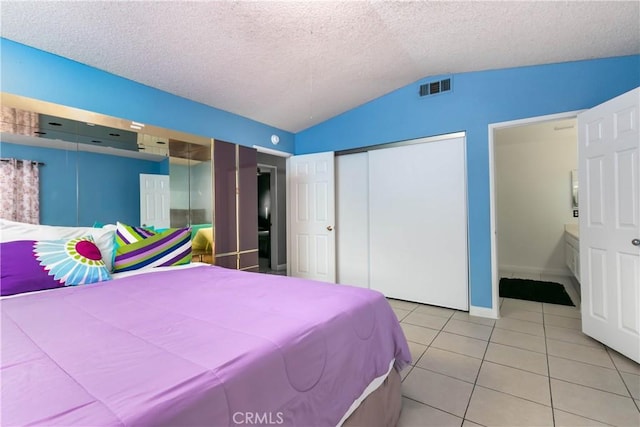 bedroom featuring ensuite bath, vaulted ceiling, a textured ceiling, a closet, and light tile patterned floors