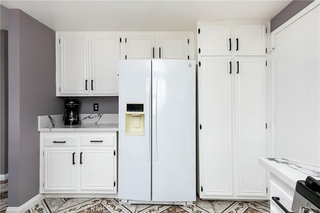 kitchen featuring white cabinets, light stone counters, and white refrigerator with ice dispenser