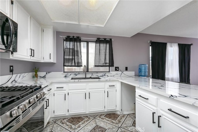 kitchen with kitchen peninsula, light stone countertops, stainless steel range, sink, and white cabinets