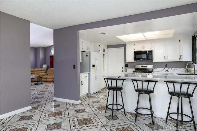 kitchen with a kitchen bar, kitchen peninsula, white refrigerator with ice dispenser, white cabinets, and stainless steel range with gas stovetop