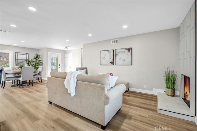 living room with plenty of natural light, light hardwood / wood-style flooring, and a tiled fireplace