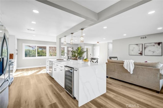 kitchen featuring decorative light fixtures, wine cooler, sink, white cabinetry, and an island with sink