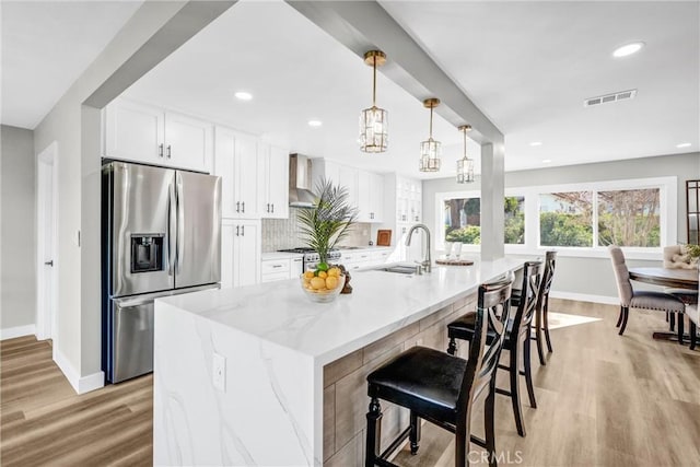 kitchen with a spacious island, white cabinets, wall chimney exhaust hood, and stainless steel appliances