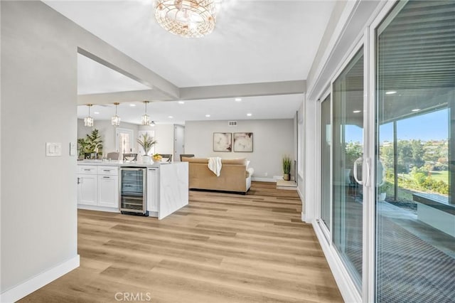 interior space with light hardwood / wood-style floors, kitchen peninsula, beverage cooler, hanging light fixtures, and white cabinets