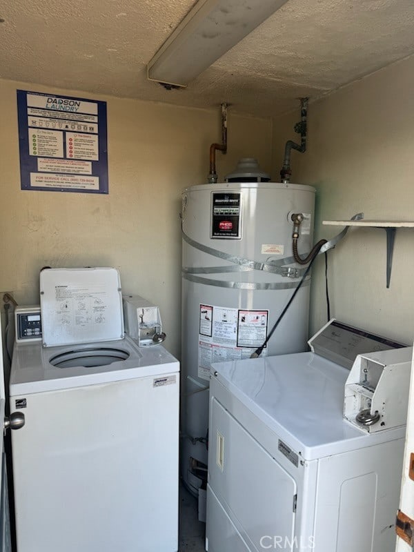 clothes washing area with washing machine and dryer, water heater, and a textured ceiling