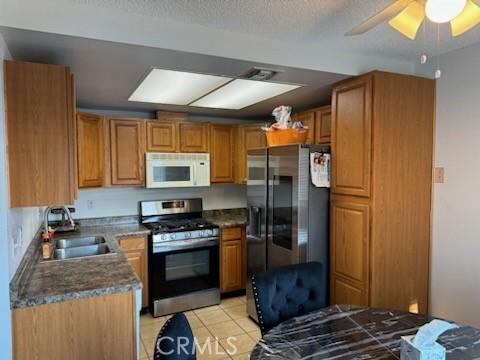 kitchen featuring sink, ceiling fan, light tile patterned floors, a textured ceiling, and stainless steel appliances