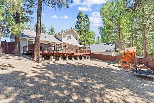 rear view of property featuring a playground, a trampoline, and a wooden deck