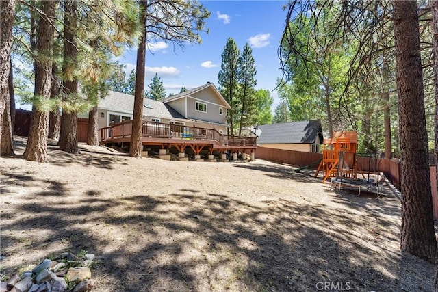 rear view of house featuring a trampoline, a deck, and a playground