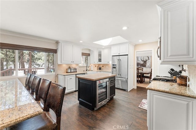 kitchen with a skylight, stainless steel appliances, a kitchen island, dark wood-type flooring, and white cabinetry